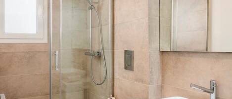 A modern bathroom with a glass-enclosed shower, a white sink, and a large mirror.