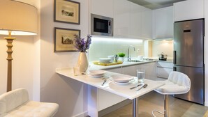 A modern kitchen with white cabinetry, a stainless steel refrigerator, a microwave, and a bar stool. - 2 Bd Apartment in the Center of Seville. Baños III (Seville)
