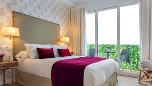 A hotel room with a large bed, two bedside lamps, a nightstand, a red rug, a balcony with a chair, and a view of greenery. - 2 Bd Apartment in the Center of Seville. Baños III (Seville)