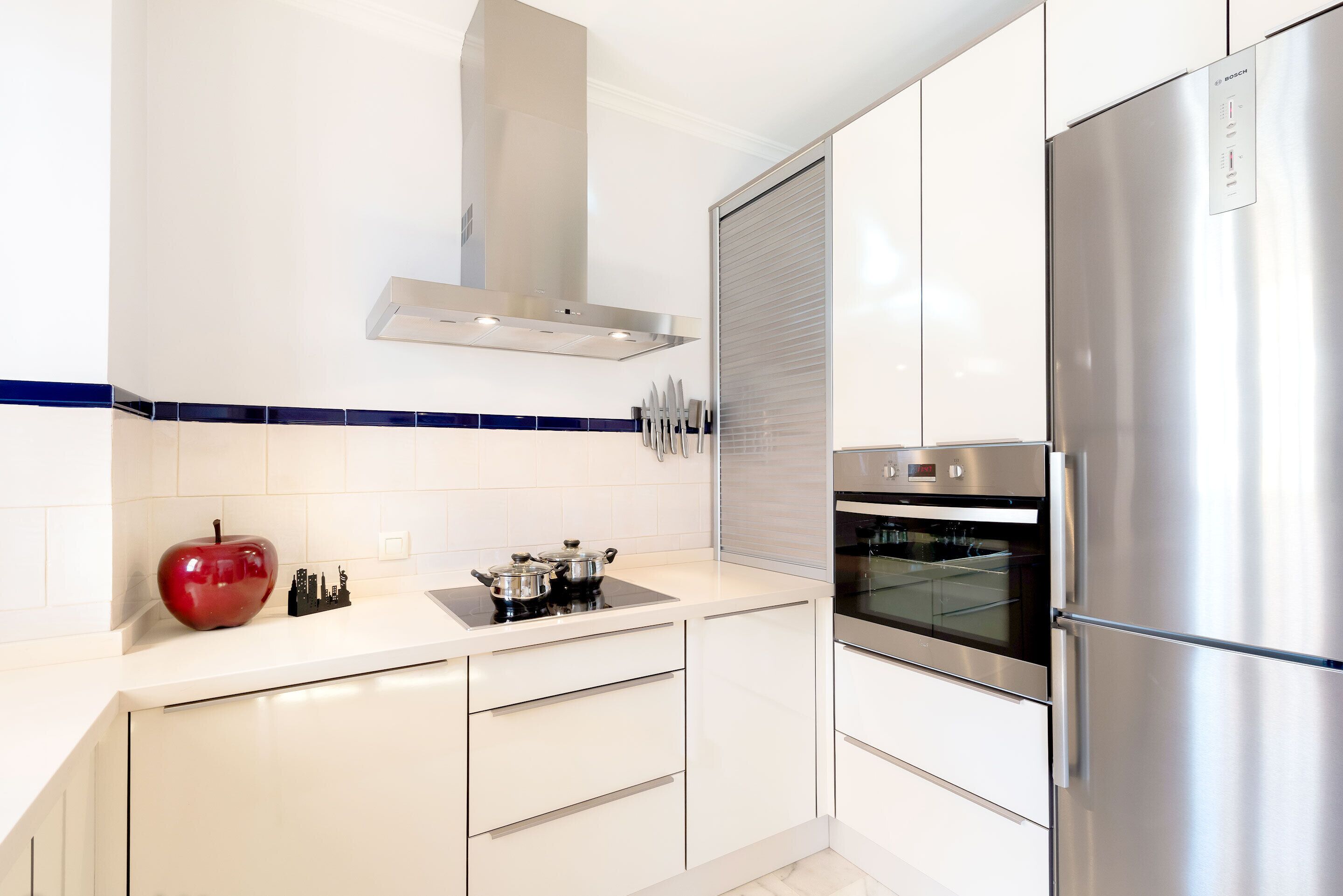A modern kitchen with stainless steel appliances, white cabinetry, and a blue-tiled backsplash.