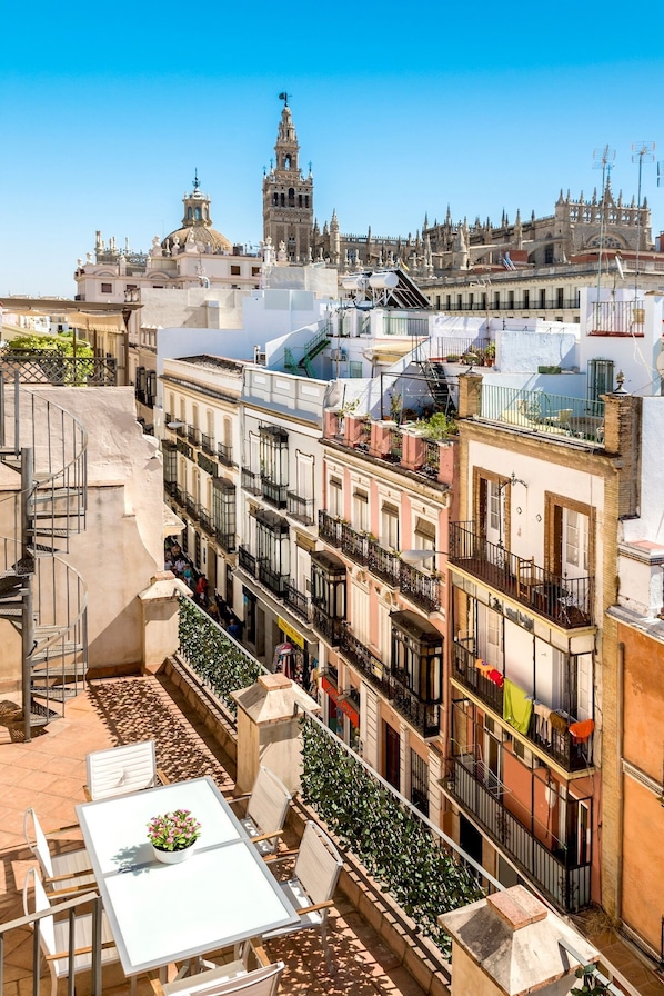 Une terrasse sur le toit avec des sièges en plein air, une vue sur des bâtiments historiques et un clocher en arrière-plan.