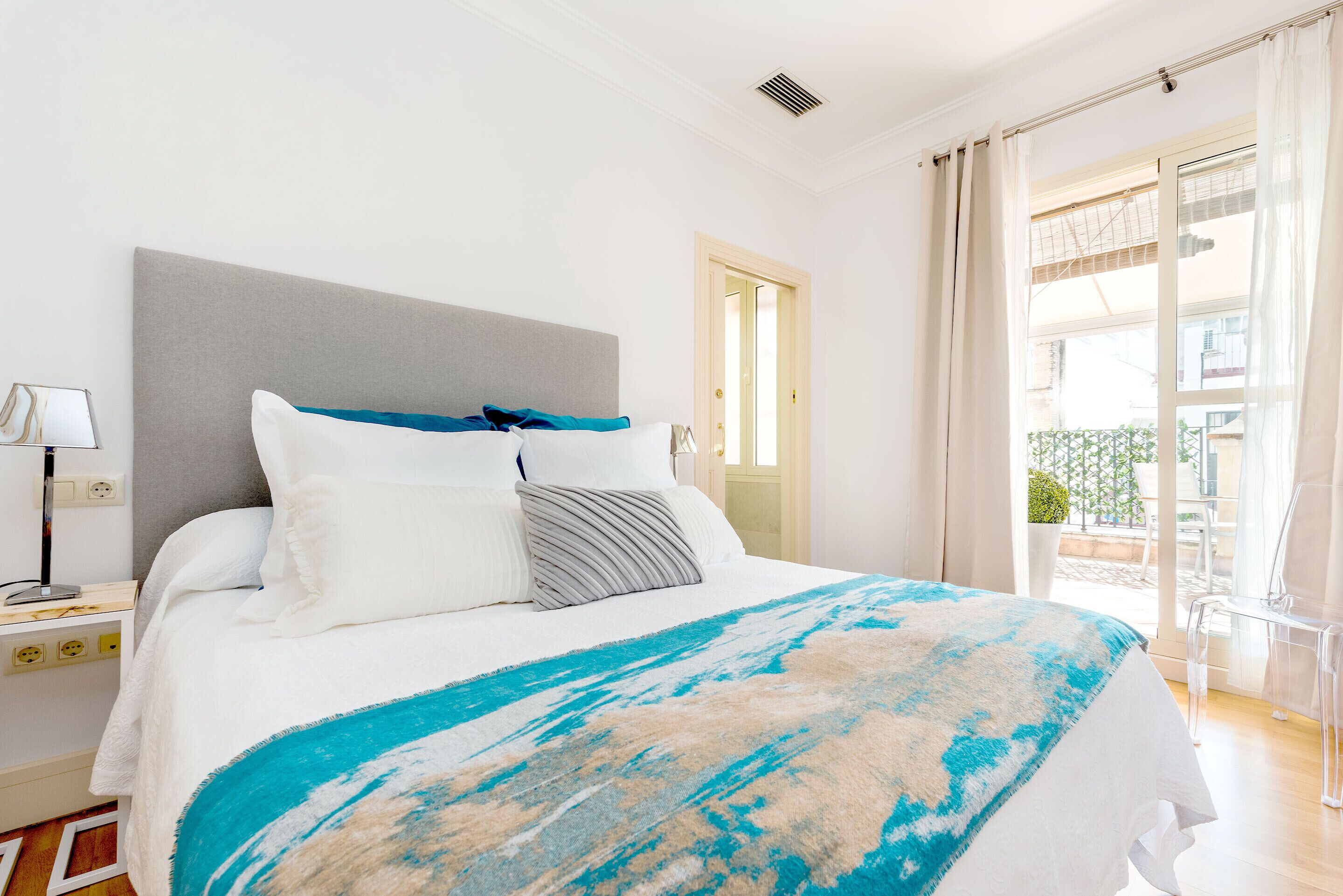 A hotel room with a bed, a nightstand, a lamp, a window with curtains, and a view of the outside.