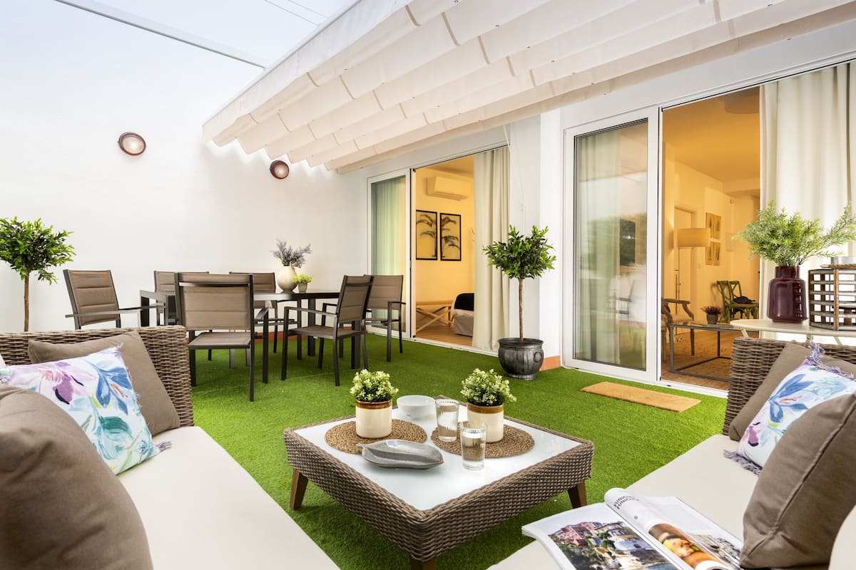 Une terrasse extérieure moderne, aménagée avec des meubles en osier, une table à manger et des plantes en pot.