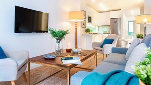 A modern living room with a flat-screen TV, a coffee table with a vase of greenery, and a sofa with cushions. - Genteel Home Baños (Seville)