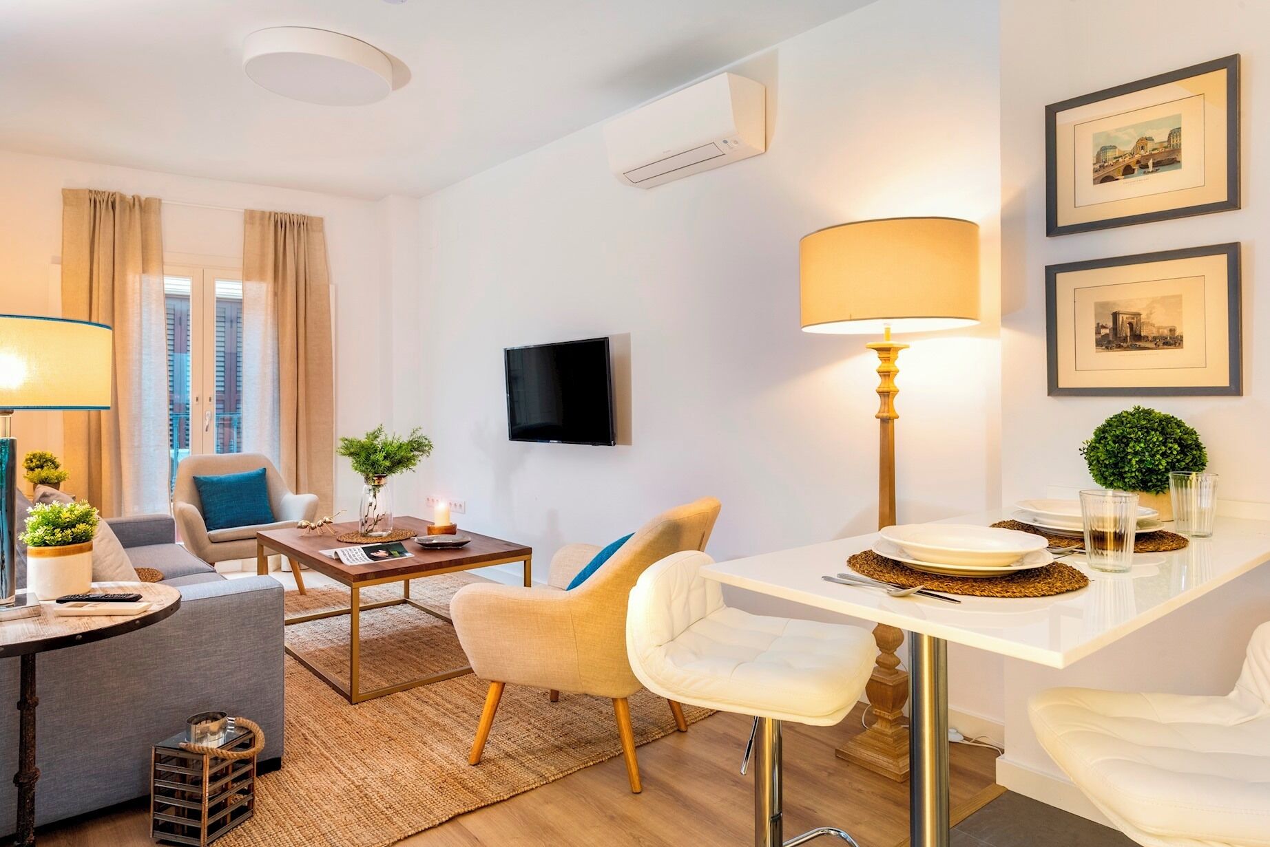 Een moderne woonkamer met een bank, stoelen, een salontafel en een eethoek met een tafel en stoelen. Er is een televisie aan de muur bevestigd en een kleine plant op de salontafel.
