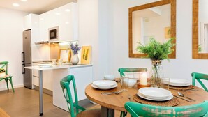 A modern kitchen with white cabinetry, a built-in microwave, and a dining area with a round wooden table set for four. - Genteel Home Baños (Seville)