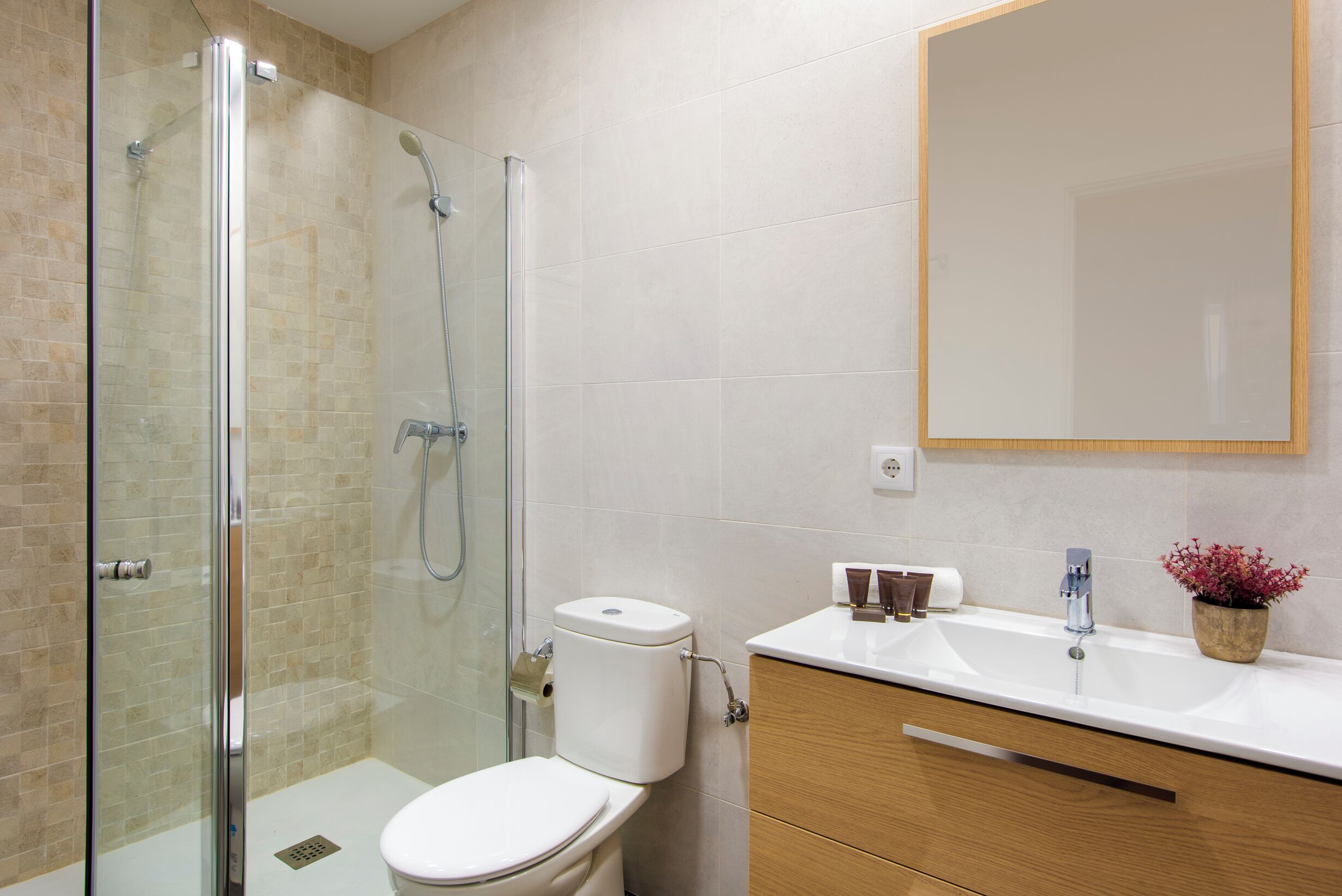 Een badkamer met een douche met glazen wand, een toilet, een wastafel met spiegel en houten kasten.