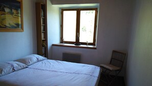Een slaapkamer met een bed, een raam, een radiator en een stoel.