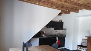 Een compacte keuken met moderne apparatuur, een eethoek met een houten tafel en stoelen, en een hoge plafond met zichtbare balken.