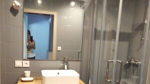 Een moderne badkamer met een grote spiegel, een witte wastafel en een douche met glazen wanden.