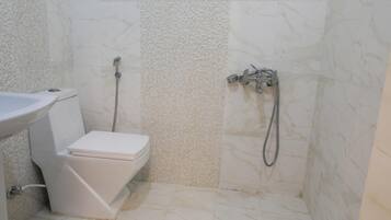 Un baño con inodoro, lavamanos y ducha con cabezal de ducha manual.