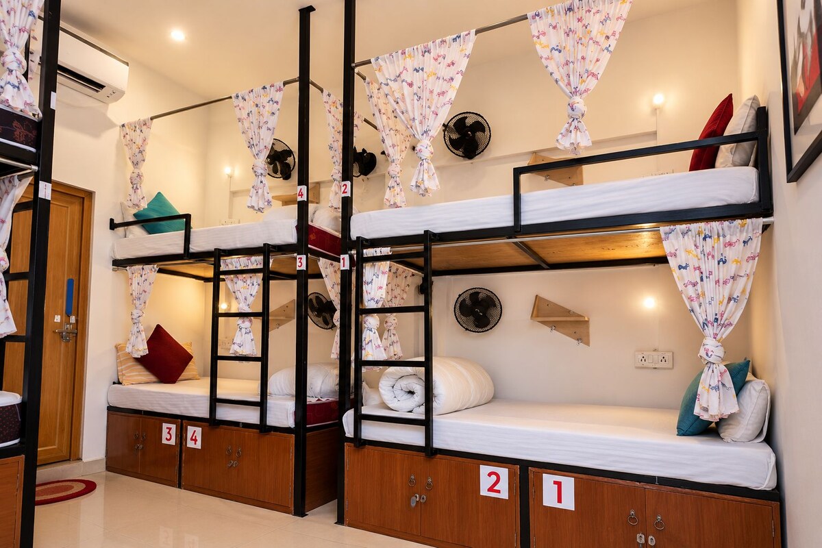 A dormitory room with bunk beds, numbered lockers, and a fan.