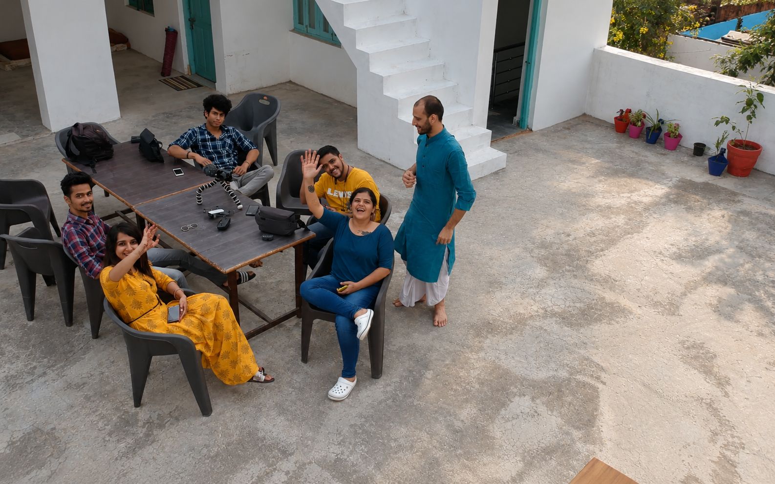 A group of people seated around a table in an outdoor setting with a concrete floor, surrounded by chairs and a staircase.