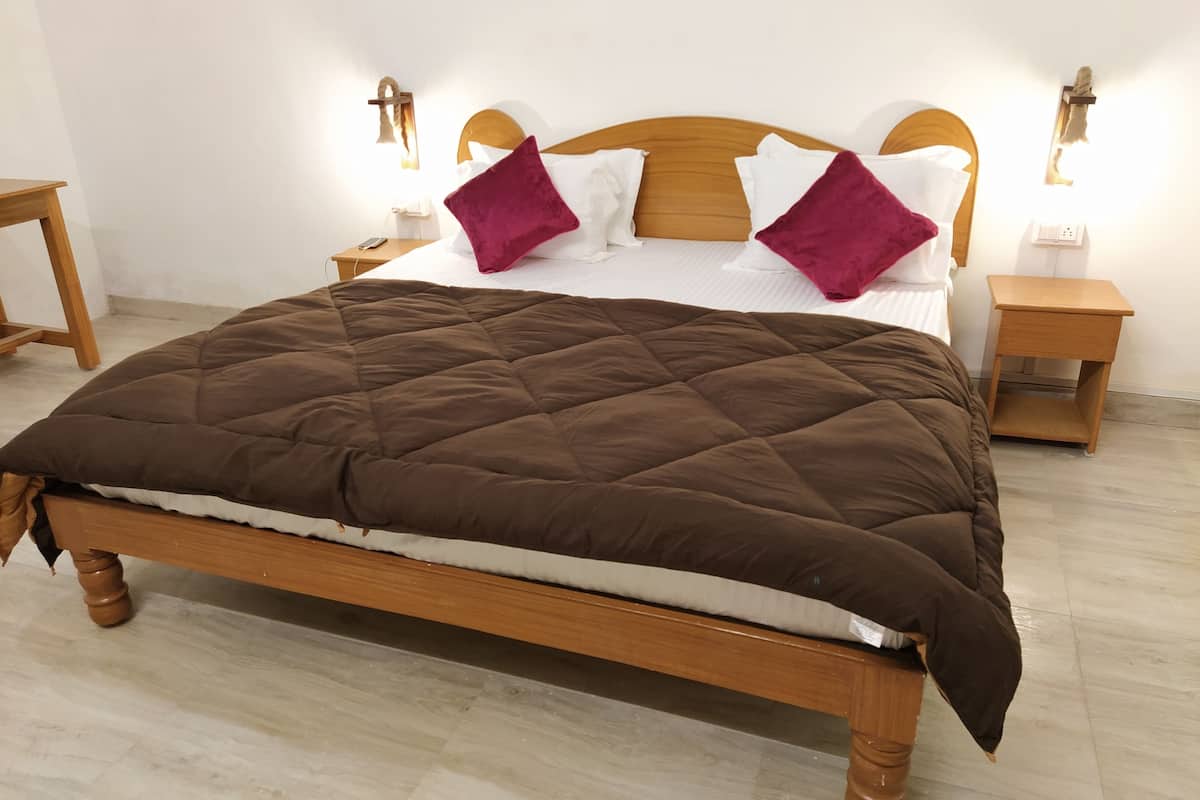 A neatly made bed with a brown quilt, white linens, and two purple pillows. There are two wooden nightstands with lamps on either side of the bed.