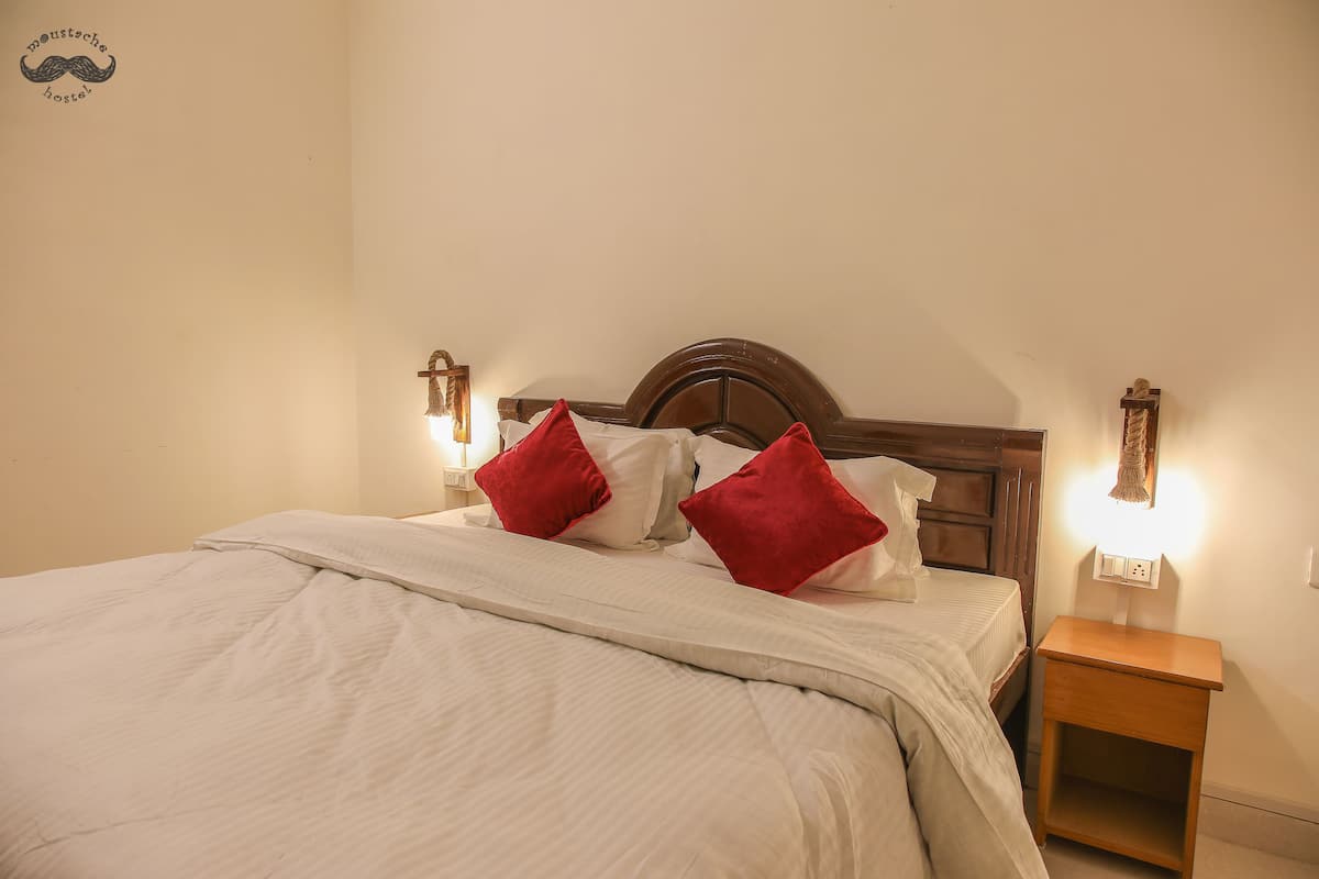 A neatly made bed with white bedding and two red pillows, a wooden headboard, and bedside lamps on either side.