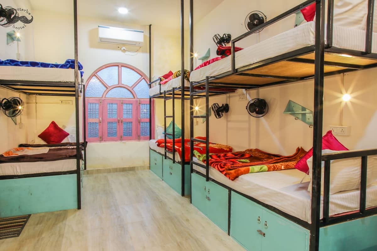 A dormitory room with bunk beds, a window, and a fan.