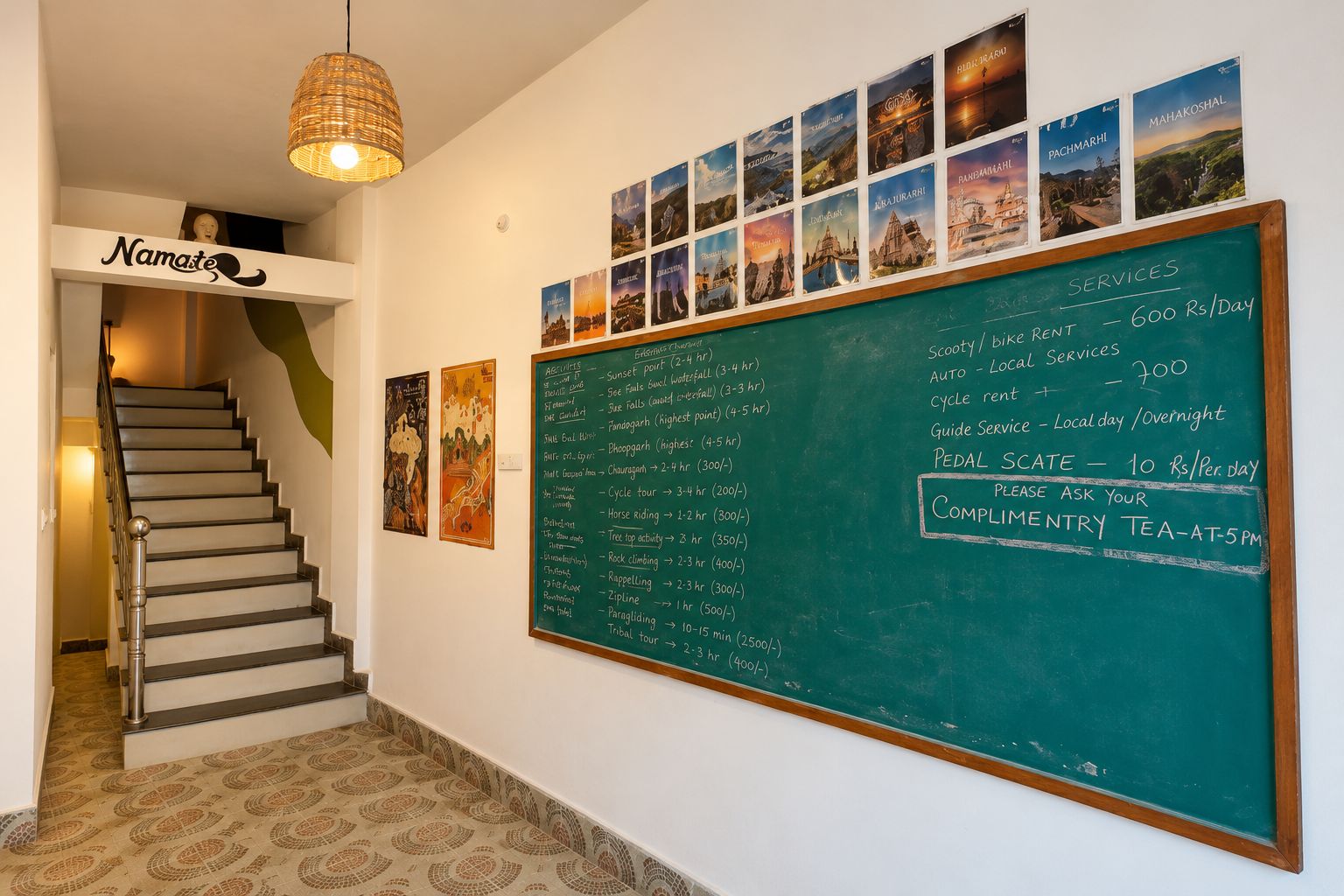 Un pasillo de hotel con una escalera, una pizarra fijada a la pared que enumera servicios y precios, y una serie de fotografías enmarcadas.