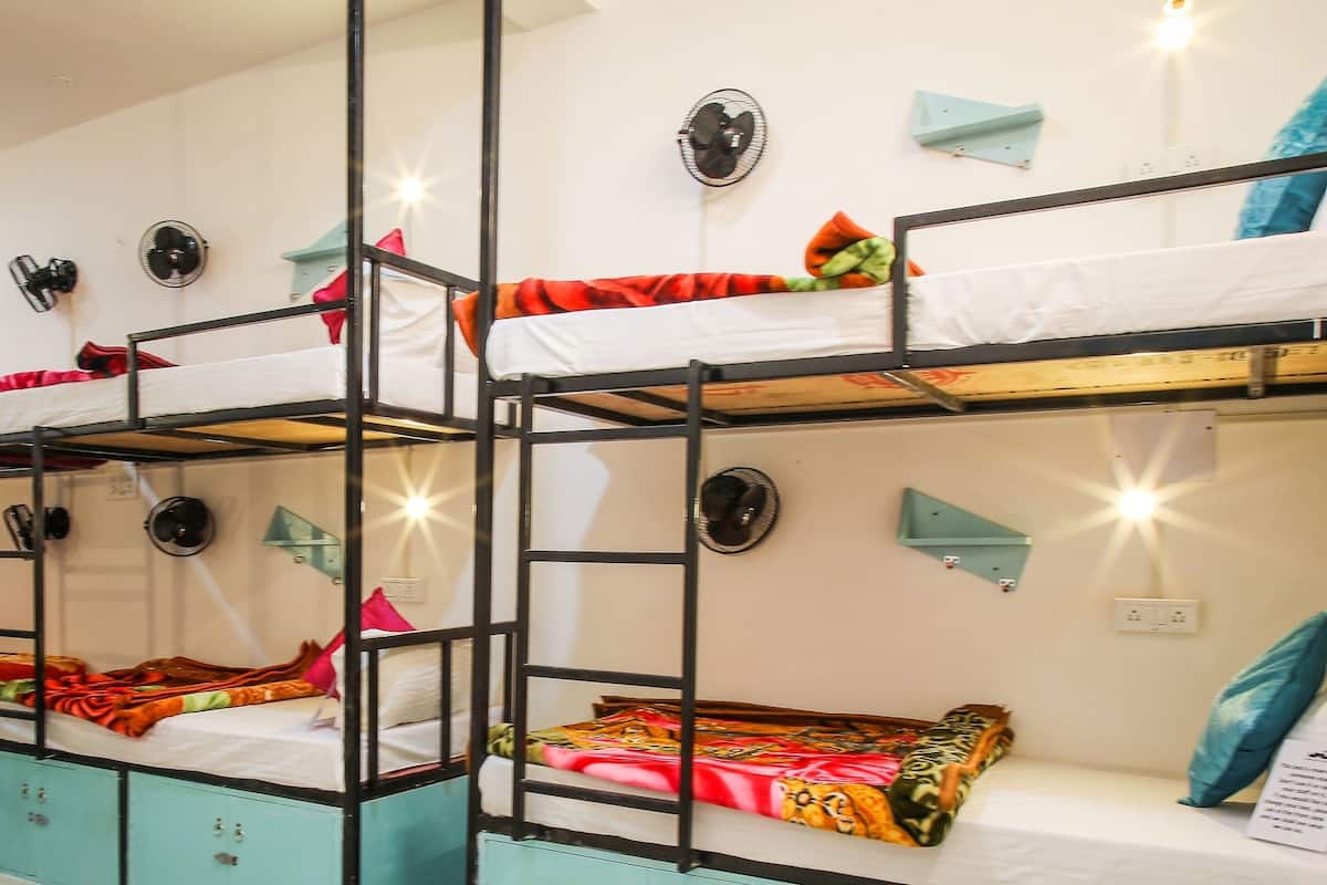 A dormitory room with bunk beds, teal cabinets, and wall-mounted fans.