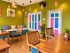 A room with a green wall, a wooden dining table, and a bench with cushions. - Moustache Khajuraho - Hostel (Rajnagar)