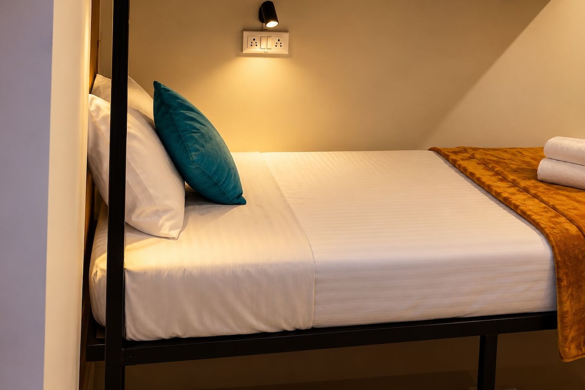 A single bed with white bedding, a teal pillow, and a brown throw blanket.