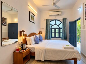 A hotel room with a bed, bedside table, mirror, window with curtains, and an air conditioning unit.