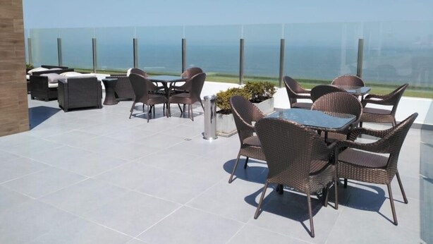 Une terrasse sur le toit avec des sièges extérieurs, une balustrade en verre et une vue sur l’océan.