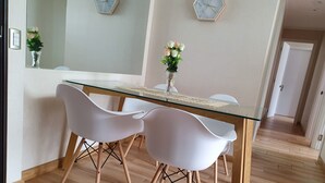 Un coin repas moderne avec une table à plateau en verre, deux chaises blanches et un vase de fleurs.