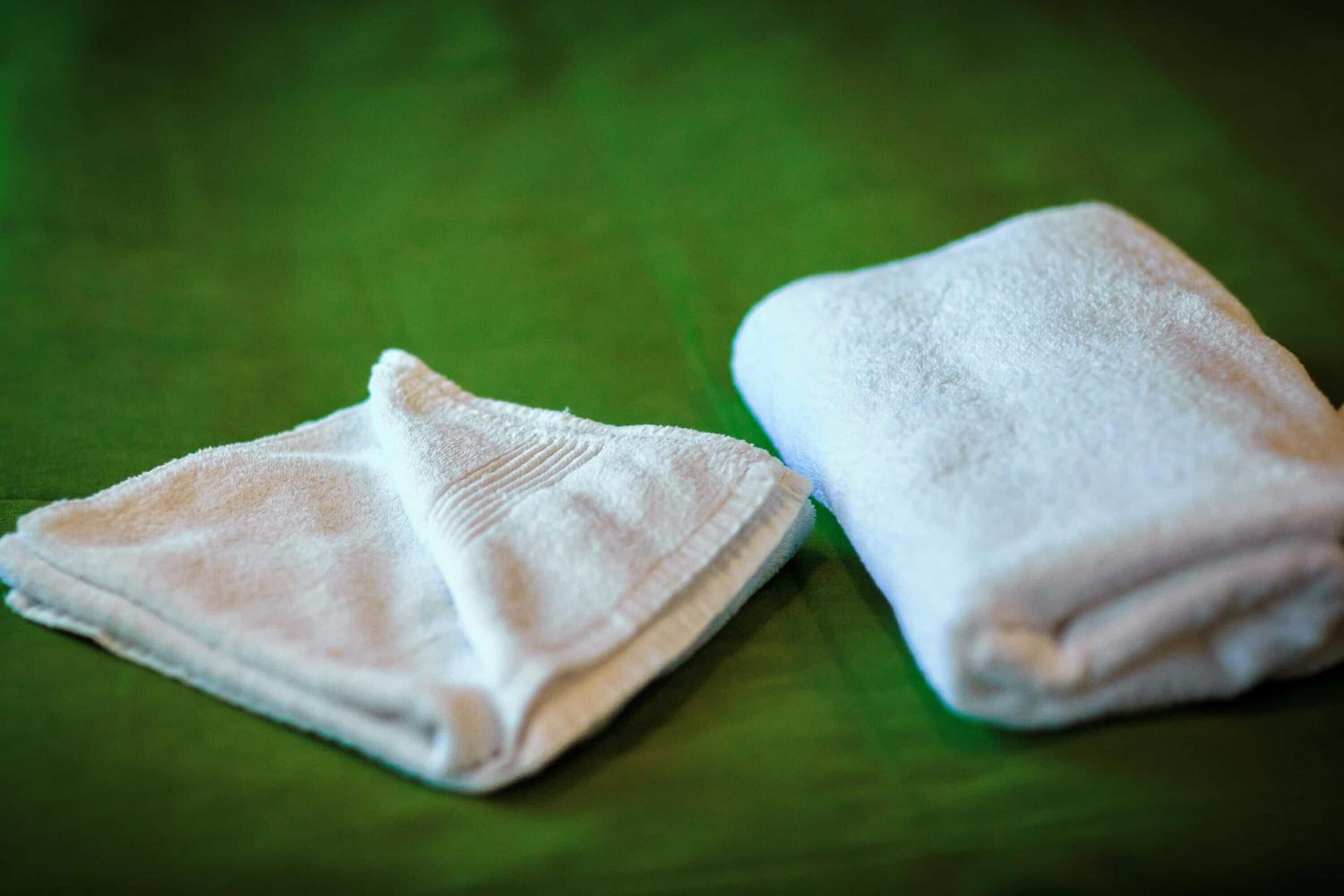 Two folded white towels on a green surface.