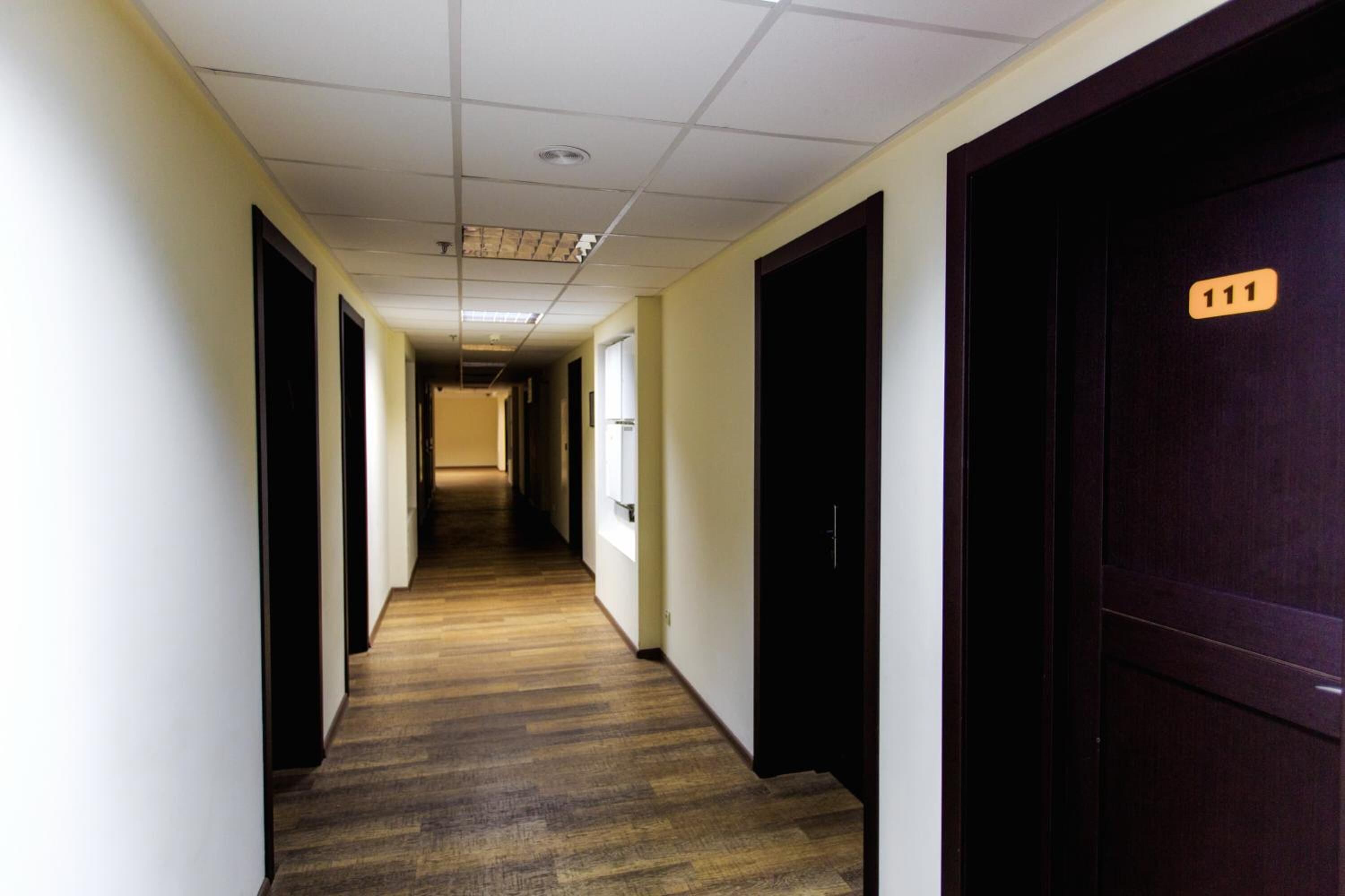 Un long couloir étroit, doté d’un plancher en bois et de portes sombres de part et d’autre.