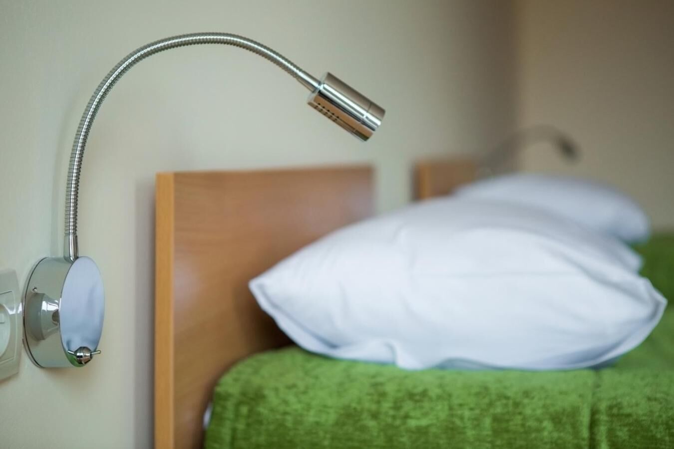 A bed with a green blanket and white pillow, a wooden headboard, and a wall-mounted adjustable shower head.