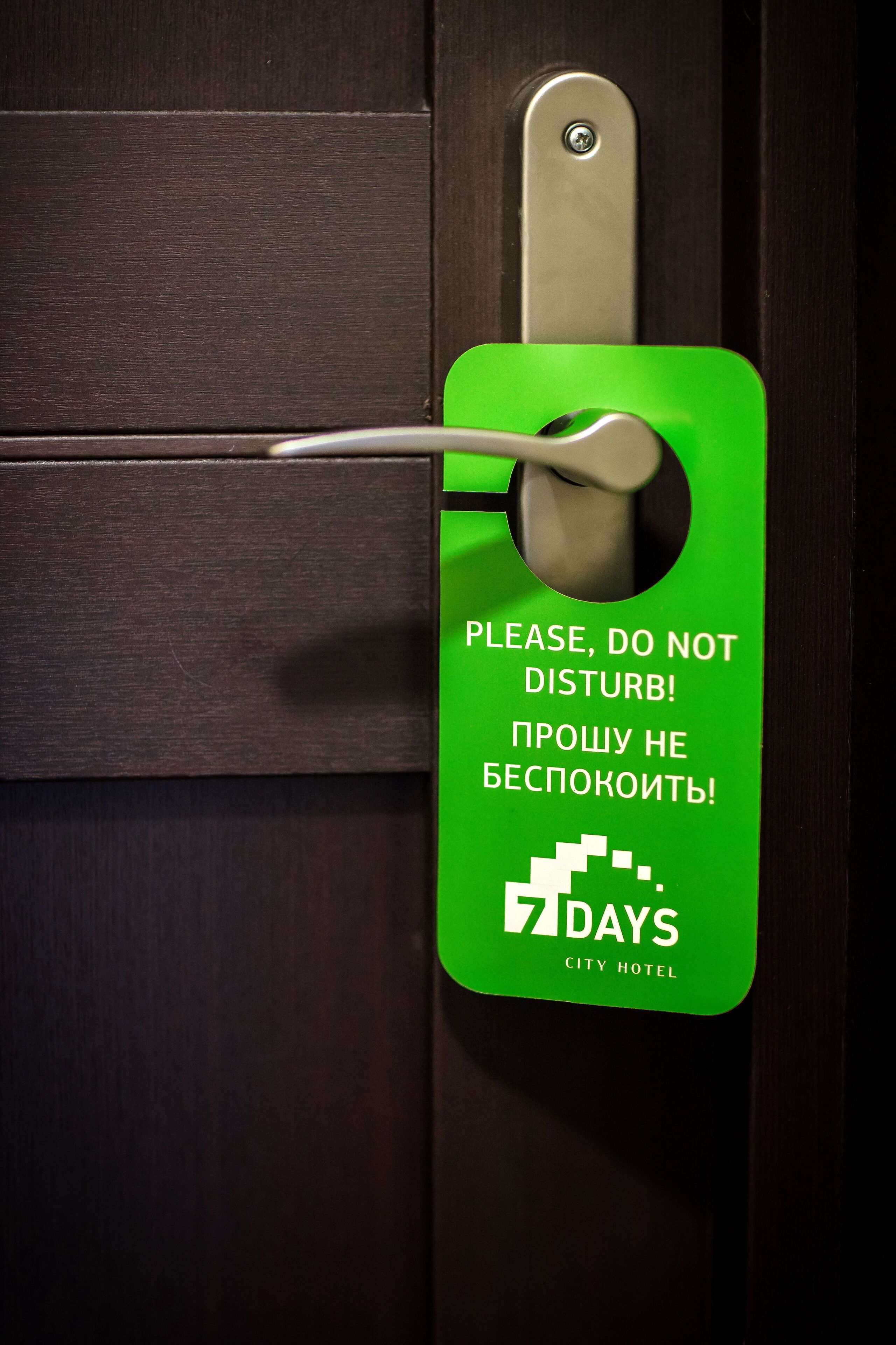 Una puerta con un letrero verde que dice “PLEASE, DO NOT DISTURB! PROSZU NE BESPOKOITIE!” y “7 DAYS CITY HOTEL”.