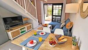 A modern living space with a dining area, a TV, and a staircase.