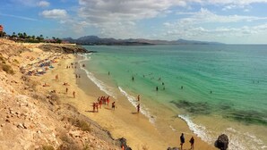A beach with clear turquoise waters, people sunbathing and swimming, and a rocky shoreline.