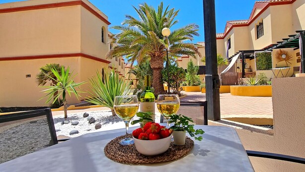 A table with a bowl of strawberries and two wine glasses on a terrace with a view of buildings and palm trees.