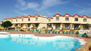 A hotel with a pool area, multiple lounge chairs, and a clear blue sky.