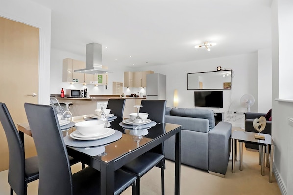 A modern hotel room with a dining area, kitchenette, and a seating area with a flat-screen TV.