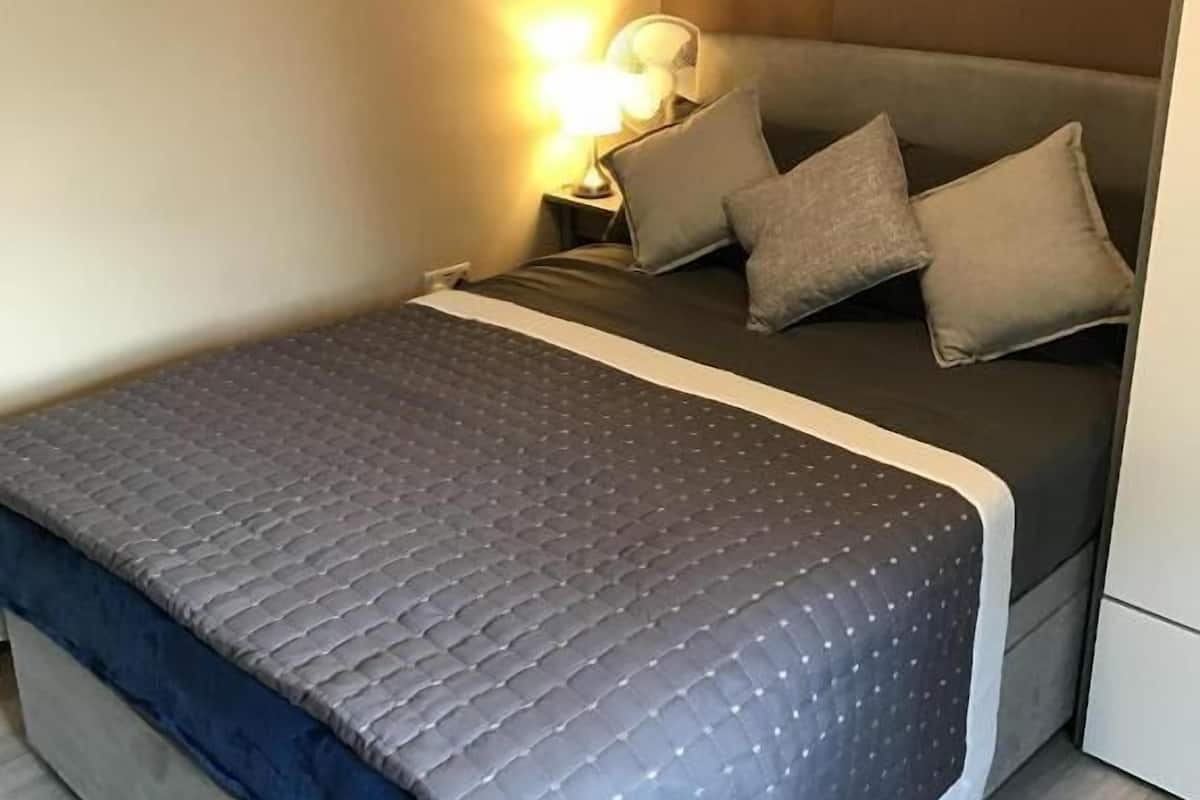 Una cama con cubierta acolchada, almohadas, una lámpara de noche y suelo de madera.