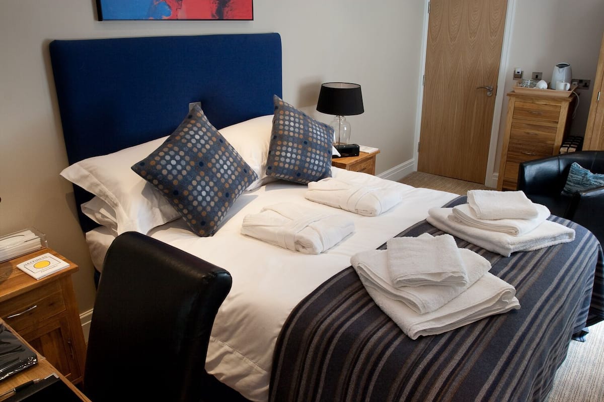 A neatly made bed with pillows, a lamp, and towels on a bedside table.