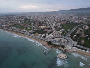 Vista aérea de una ciudad costera con un paseo marítimo destacado, una rotonda central y una combinación de edificios residenciales y comerciales.