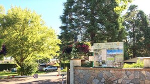 A stone wall with a signboard, a car parked nearby, and trees in the background. - Camping Moulin du Roy (Revel)