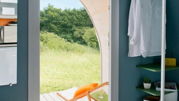 A room with a large sliding door leading to a deck, a white towel rack, and a wooden chair. - Camping Moulin du Roy (Revel)