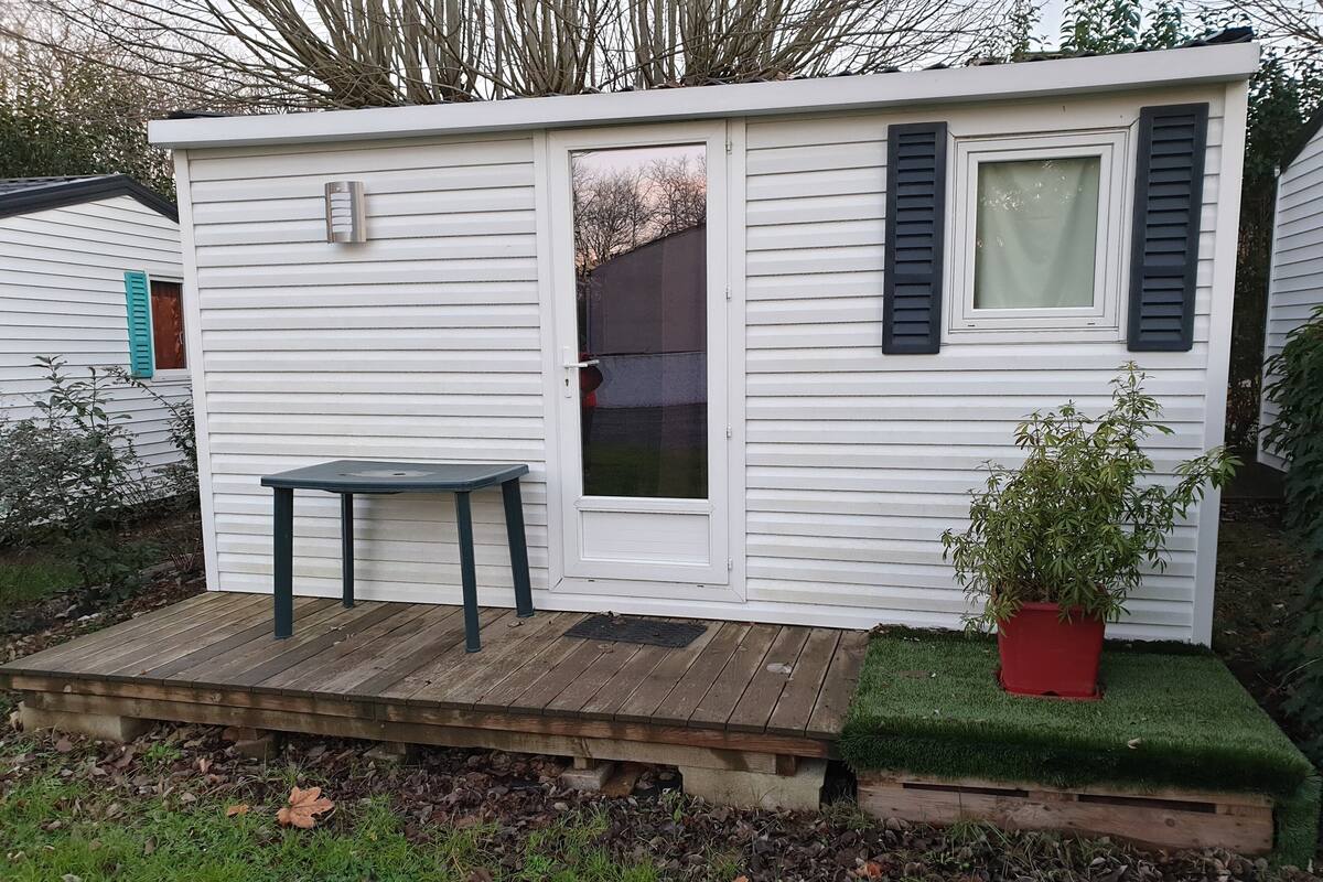 Une petite cabane à un seul étage, dotée d’une terrasse en bois, d’une table et d’une plante en pot.