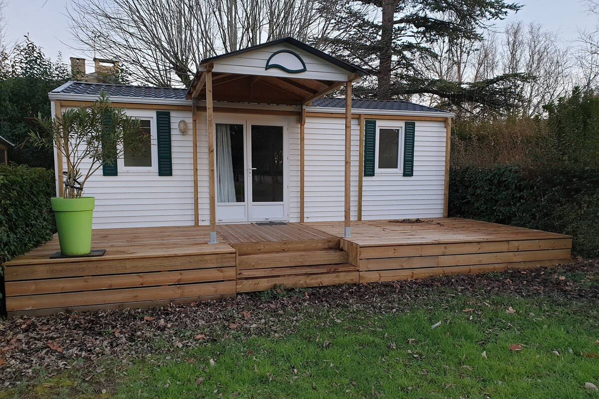 Une petite cabane en bois avec un porche, une plante verte en pot et une porte dotée d’une fenêtre.