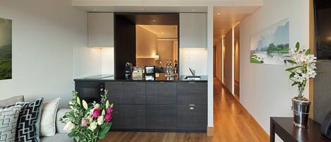 Uma sala de estar moderna, com um sofá, uma mesa de centro e um vaso de flores. Uma cozinha visível ao fundo, com bancada e armários.