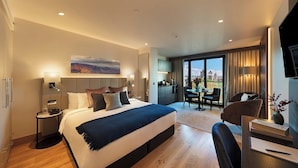 A modern hotel room with a large bed, a desk, and a dining area with a view. - Tower Suites by Blue Orchid (London)