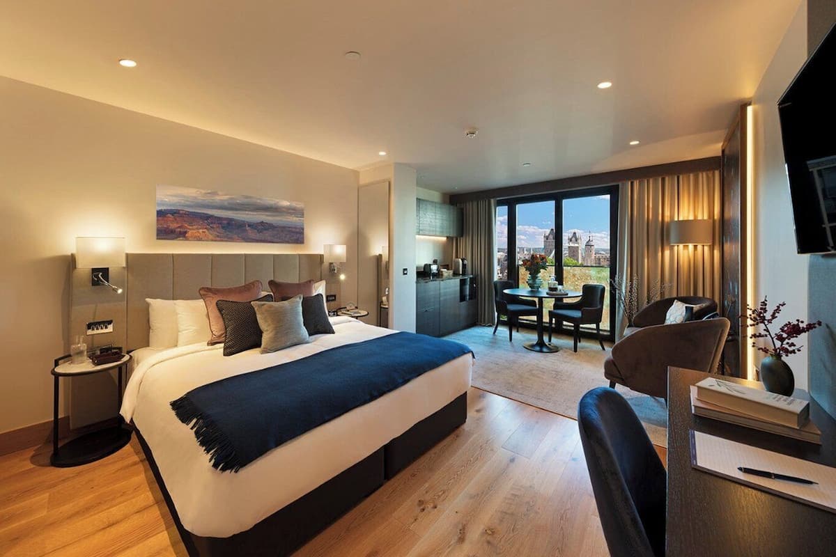 A modern hotel room with a large bed, a desk, and a dining area with a view.
