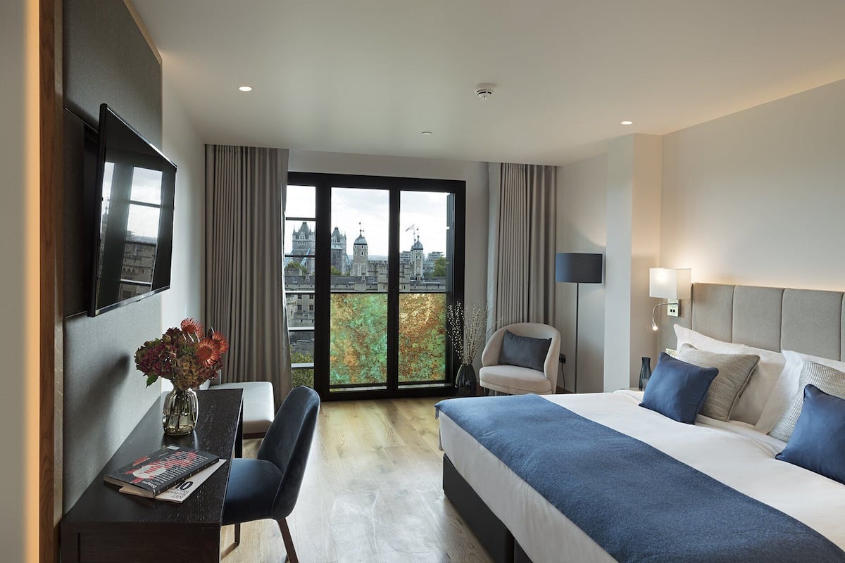 A hotel room with a bed, a desk, a chair, a TV, and a large window with a city view.