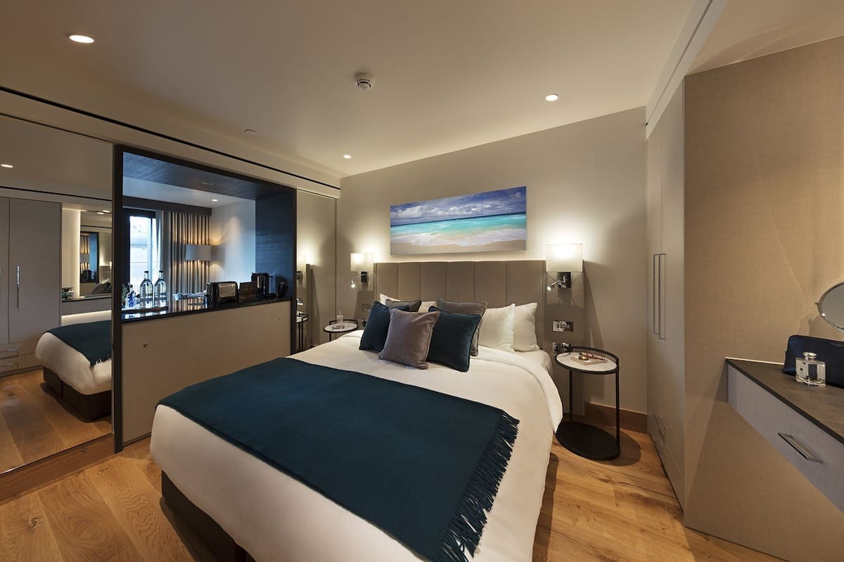 A modern hotel room with a large bed, bedside tables, a desk, and a mirror.
