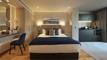 Quarto de hotel moderno com cama grande, mesas de cabeceira, escrivaninha e cozinha compacta.