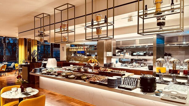 A modern restaurant with a central bar area, yellow chairs, and a marble countertop. - Tower Suites by Blue Orchid (London)